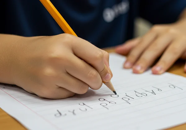 Child's hand writing 'b' and 'd' letters reversed.